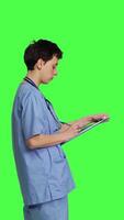 Profile Confident hospital nurse taking notes for the next medic appointment, standing over greenscreen backdrop. Medical assistant with uniform writing patient information on clipboard papers. Camera B. video