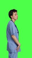 Profile Stressed nurse checking time on watch and waiting for patient to arrive at checkup examination, being impatient against greenscreen backdrop. Medical assistant with scrubs and stethoscope. Camera B. video