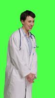 Side view Portrait of general practitioner laughing at something against greenscreen backdrop, feeling joyful and confident with her healthcare expertise. Woman medic in white coat smiling in studio. Camera B. video