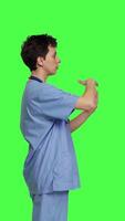 Medical assistant giving timeout symbol against greenscreen backdrop, showing limits and asking for a break. Nurse doing pause or stop gesture while she wears blue scrubs. Camera B. video