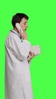 Profile Physician answering landline phone call against greenscreen backdrop, talking to patients about checkup appointments. Medic having remote discussion on retro telephone with cord. Camera B. video