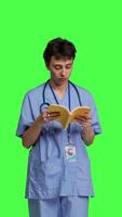 Front view Medical assistant reading a literature book against greenscreen backdrop, enjoying healthcare industry lecture to acquire new expertise. Nurse paying attention to medicine manual at work. Camera B. video