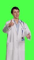 Front view Cheerful medic doing thumbs up symbol against greenscreen backdrop, expresses positivity with like sign. General practitioner with coat giving approval and being satisfied with success. Camera B. video