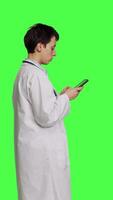 Profil Arzt navigieren auf Sozial Medien Apps zu Text Menschen, steht gegen grüner Bildschirm Hintergrund. Medizin im Weiß Mantel Surfen Websites online, Herstellung Untersuchung Termine. Kamera b. video