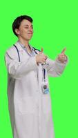 Side view Cheerful medic doing thumbs up symbol against greenscreen backdrop, expresses positivity with like sign. General practitioner with coat giving approval and being satisfied with success. Camera B. video
