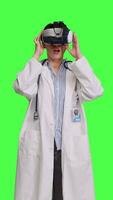 främre se läkare användningar virtuell verklighet interaktiv lins på headsetet i studio, checkar diagnos med artificiell intelligens tre dimensionell verktyg. läkare Arbetar med vr glasögon mot grönskärm. kamera b. video