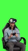 Front view Player using virtual reality glasses to have fun on cyberspace gaming competition, playing video games and winning. Gamer against greenscreen backdrop uses vr headset and controller. Camera B.