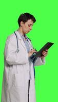 Side view General practitioner studying radiography scan results for patients with disease, stands against greenscreen backdrop. Medic examines x ray diagnosis, works with a tablet. Camera B. video