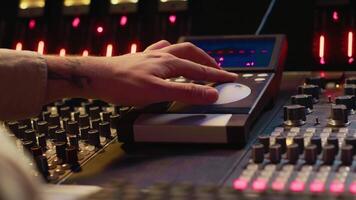 Audio technician uses mixing console and faders in control room, remote control for adjusting sound on mixer. Music producer changes volume level, creates tracks with technical equipment. Camera A. video