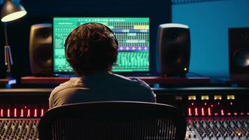 Using audio editing software, sound producer creates tunes and handling technical equipment on a control room dashboard. Technician music producer increases tracks quality. Camera A. video