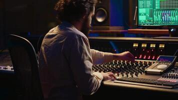 Mixing engineer focuses on blending and balancing individual tunes of a recording to create song, audio editing software in control room. Expert deals with technical aspects of sound. Camera A. video