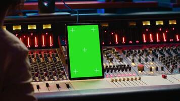 profesional audio experto mezcla y dominar pistas en música producción estudio, emprendedor botones y conmutadores en controlar habitación. sonido ingeniero grabación melodías con pantalla verde tableta. cámara una. video