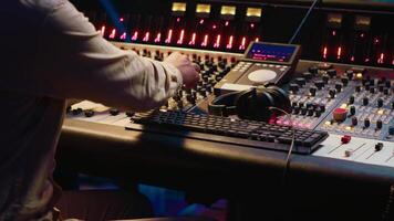 Mixing engineer pressing sliders on control desk to balance tracks and add sound effects, creating new music. Audio engineering expert works with motorized faders in professional studio. Camera A. video