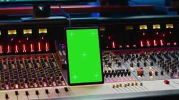 Audio expert processing sounds next to tablet with isolated mockup, working in post production with mixing console and technical gear. Producer pushing switchers and sliders. Camera A. video