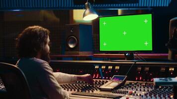 Audio specialist uses greenscreen workstation to watch tutorials and understand how to blend recorded tunes. Professional expert in tracking sounds, controls knobs and levers. Camera A. video