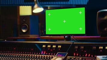 Empty professional recording studio control room with greenscreen on display, editing and processing tracks. Motorized faders, buttons and sliders operated for mix and master techniques. Camera A. video
