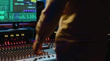 Music producer editing tracks with mixing console and audio software in studio, pressing key buttons and twisting knobs in control room. Sound engineer producing tunes and adjusting volume. Camera A. video