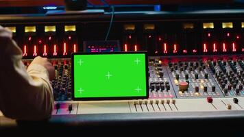 Audio expert mixing and mastering tunes on editing software next to greenscreen tablet, producing and recording tracks by pushing buttons and faders. Sound engineer in control room. Camera A. video