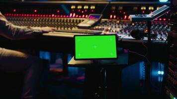 Sound designer processing and recording tracks in control room, using mixing console and sliders to adjust volume level. Technician working with greenscreen tablet in professional studio. Camera A. video