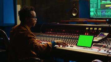 Sound engineer expert recording audio tracks next to tablet mockup, adding sound effects on songs with mixing console. Producer pressing buttons and sliders in control room. Camera A. video