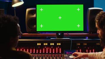 Diverse skilled artists working with isolated mockup display on pc, mixing and mastering tracks before creating a hit. People operating on control room console with knobs and sliders. Camera A. video