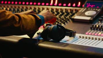 afrikansk amerikan ljud ingenjör använder sig av hörlurar till lyssna till audio inspelningar i posta produktion, justeras volym nivåer med redigering programvara gränssnitt. expert- i studio kontrollera rum. kamera a. video