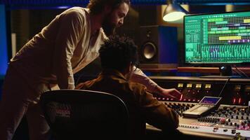 Tracking engineer collaborating with musician to edit sounds in studio control room, recording tunes to create a new album. Audio expert operating audio mixer and controller. Camera A. video