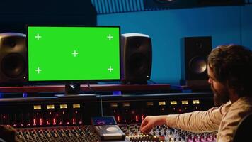 Team of music engineer and artist recording tracks on greenscreen, processing sounds to create a new song. Musician working closely with producer to make high quality tunes. Camera A. video