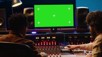 Diverse producers mixing and mastering tracks with mockup display on computer, recording before adding effects in post production. Artist and sound engineer twisting control desk knobs. Camera A. video