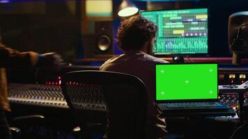 Team of artist and music producer work with mockup display, processing and mixing sounds in professional studio control room. Experts producing tracks by using technical equipment. Camera A. video