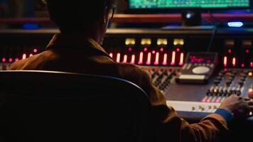 African american sound engineer recording and editing tracks in post production, using mixing console with knobs and switchers. Skilled audio technician producing new music in studio. Camera A. video