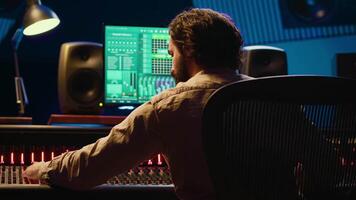 Sound designer mixing and mastering tracks on audio console in control room, using daw software on computer and editing files. Technician creating new music in professional studio. Camera A. video