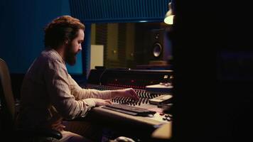 Portrait of sound engineer recording audio and editing with mixing console, twisting knobs on panel board in control room. Audio technician working on mix and master in professional studio. Camera B. video