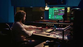 Sound engineer mixing and mastering tracks in professional recording studio, working with daw software and pushing sliders to adjust volume levels and edit audio recordings. Control room. Camera B. video