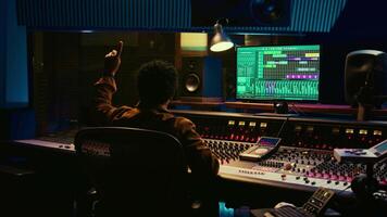 African american audio engineer counting down singer in sound booth, preparing to record and process tracks in control room. Producer twisting knobs and faders to enhance tune quality. Camera B. video