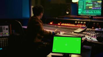 African american tracking engineer works with greenscreen, operates audio console with moving faders and colored meters. Specialist pressing buttons and faders to edit audio recordings. Camera B. video