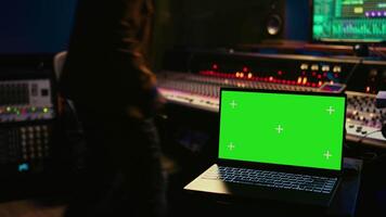 Skilled audio technician processing and mixing sounds next to mockup display on laptop, using variety on knobs, buttons and sliders to edit audio recordings and produce new music. Camera B. video