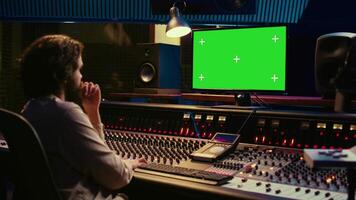 Sound designer watches online tutorials via greenscreen monitor to mix and master tracks and create music for his album. Audio engineer producing songs by twisting knobs and pushing faders. Camera B. video