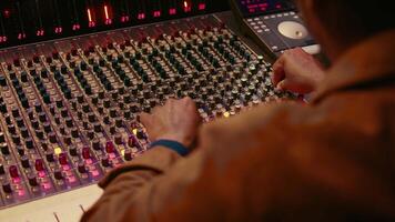 Audio technician producing new music at mixing console in control room, twisting knobs, pressing sliders and switchers. Producer working on processing and editing sounds quality. Camera B. video