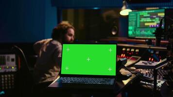 Sound designer uses audio mixer and greenscreen layout in professional studio, adjusting volume levels while pressing buttons on desk. Control room equipped with technical recording gear. Camera B. video