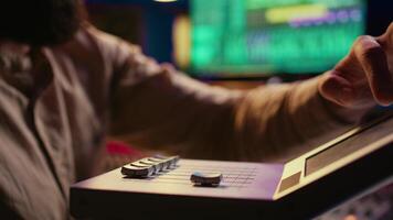 Sound engineer operating on motorized faders controller in professional studio, editing and mixing tracks to create a song. Audio technician works with sliders and soundboard panel. Camera B. video