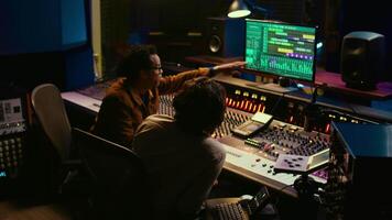 Diverse people processing and mixing sounds on audio console, adding sound effects and working on creating new tracks. Artist and technician producing a hit song, daw software. Camera B. video