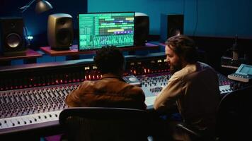 Audio expert and musician mixing and mastering tracks on control room console in studio, recording and editing tunes in music post production. Skilled artist and sound engineer. Camera B. video