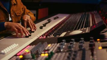 African american producer uses control desk with automatic equalizer, mixer and sliders to edit tracks in post production. Sound engineer processing audio recordings, mixing console. Camera B. video