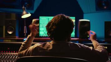 Cheerful energic audio engineer dancing on his own music creation in professional studio, editing a recording on mixing console and daw software. Sound designer processing tracks. Camera B. video