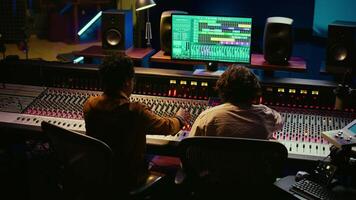 Musician and audio engineer sharing high five after creating a beautiful hit song, enjoying success in professional studio. Team of producer an artist celebrating teamwork in control room. Camera B. video