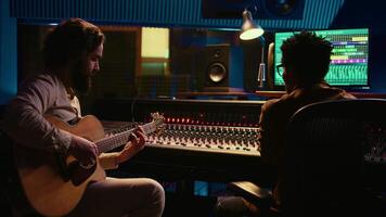 musicista e suono ingegnere registrazione chitarra melodie nel controllo camera a professionale musica produzione studio. artista giocando elettro acustico strumento, vivere prestazione nel insonorizzato spazio. telecamera b. video