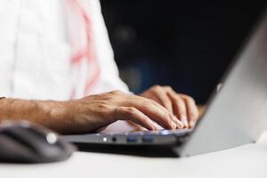 Selective focus on hands of a Middle Eastern person typing, taking notes on a minicomputer while staying connected wirelessly. Close-up shot of a person utilizing a modern digital laptop. photo