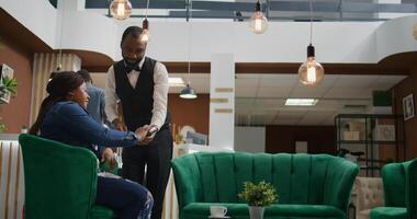 Woman paying for cup of coffee in hotel lobby, using credit card to buy drink from bar service. African american traveller making pos payment while waiting to register into room on holiday. photo