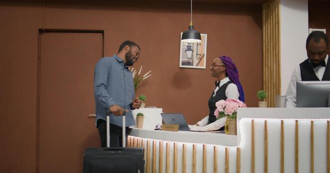 Young man does check in at reception, entering five star resort and signing registration papers at front desk in lobby. Hotel concierge employee greeting traveller at hotel, great services. photo